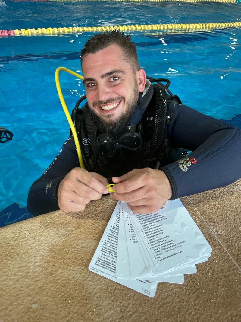Teo, instructor Atlantis-Scuba, zâmbind la marginea bazinului Plaisir, cu fișa de exerciții